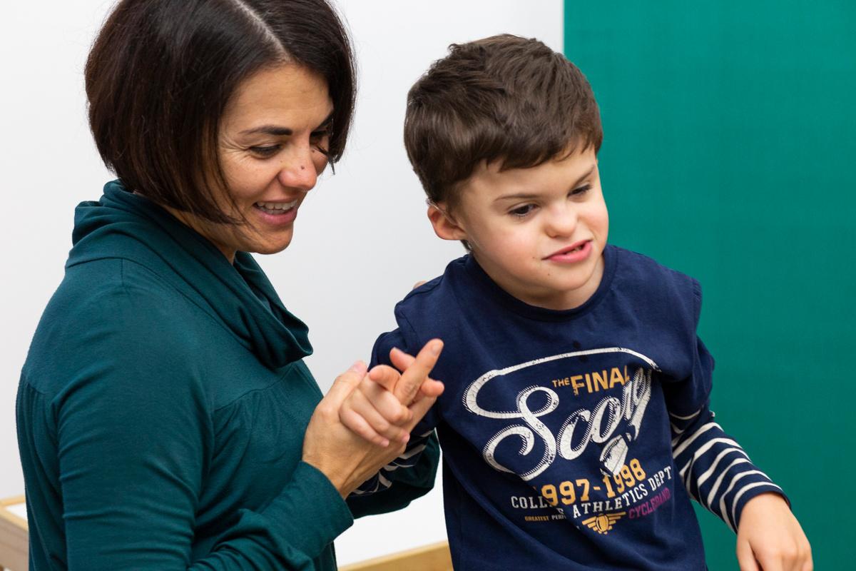Mamma Samuela prende per mano Agostino, bambino di 8 anni con sidrome di Charge seguito nel Centro Nazionale di Osimo. Entrambi sorridono.
