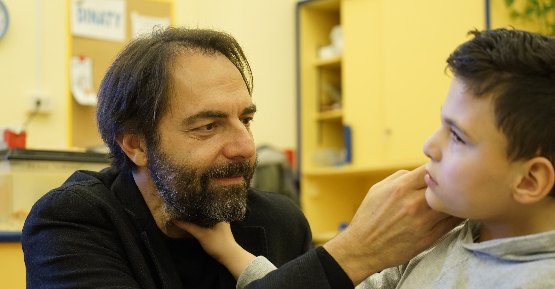 Neri Marcorè fa una carezza sul viso del piccolo Francesco, che a sua volta sta esplorando il suo volto con la mano