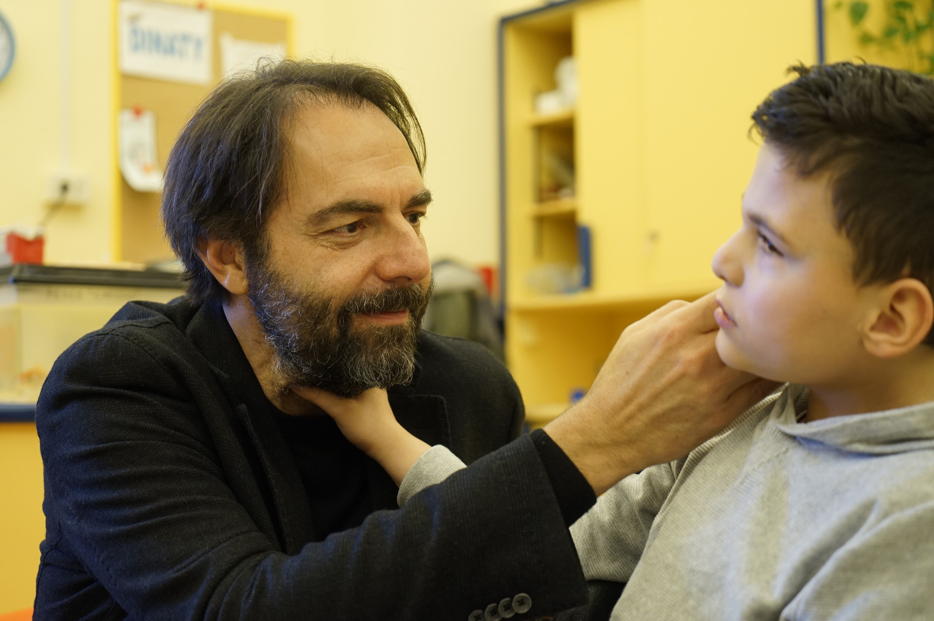 Neri Marcorè fa una carezza sul viso del piccolo Francesco, che a sua volta sta esplorando il suo volto con la mano