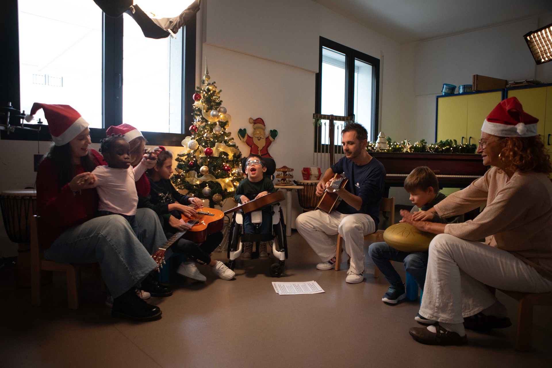 Nella foto compaiono i bimbi protagonisti della campagna di Natale: Nicola, Aurora, Princess e Matteo. Sono seduti in cerchio accanto a un albero di Natale addobbato e sono insieme ad alcuni operaotri della Lega del Filo d'Oro.