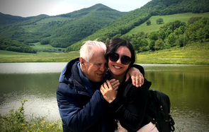 Tanya, volontaria della Lega del Filo d'Oro, abbraccia Angelo, utente sordocieco anziano, entrambi sorridono e si trovano in riva a un lago, immersi nel verde 