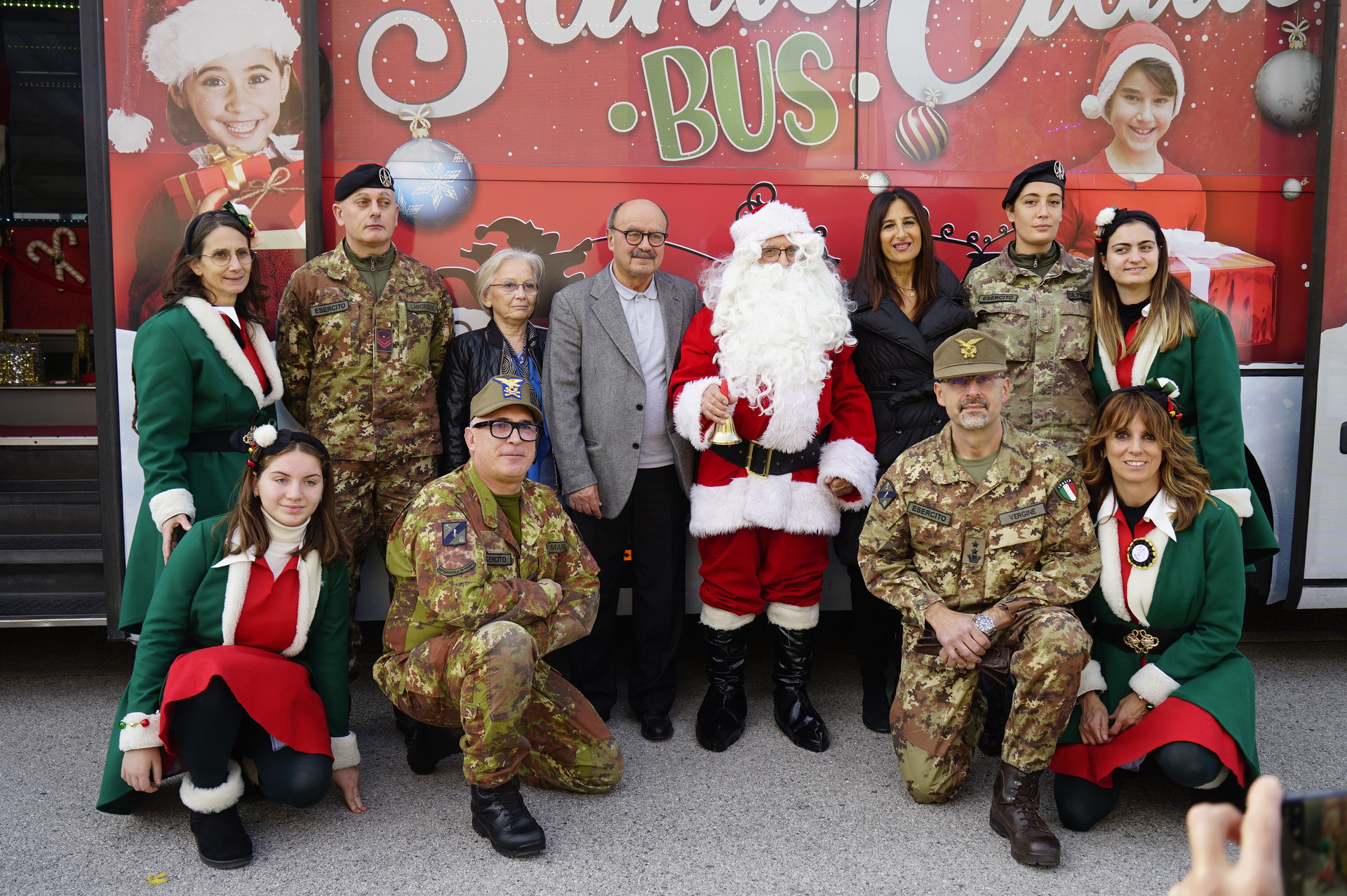 Il presidente Rossano Bartoli posa sorridente accanto a Babbo Natale, volontari e rappresentanti delle forze armate. 