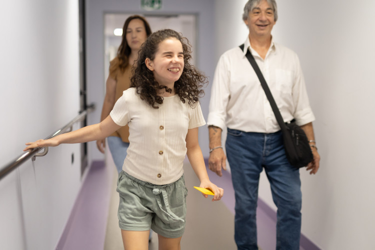 Giulia, bambina utente della Lega del Filo d’Oro, cammina sorridendo in un corridoio della sede nazionale, accompagnata dalla sua famiglia.