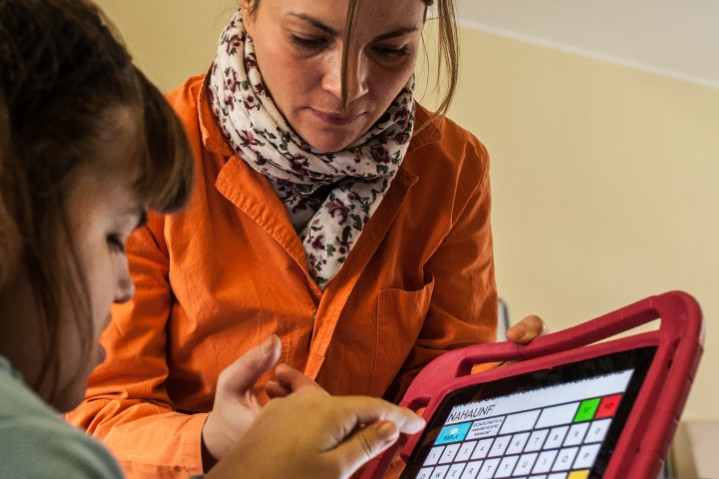 Una giovane utente impara a comunicare grazie a un tablet, con la guida dell'educatrice al suo fianco