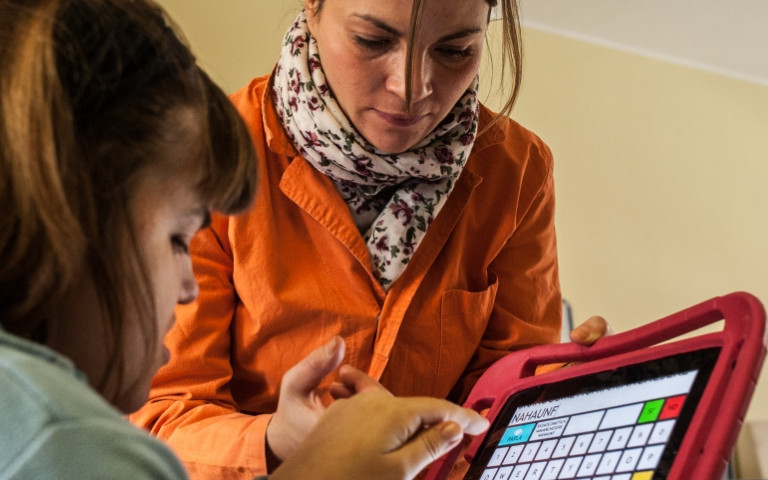 Una giovane utente impara a comunicare grazie a un tablet, con la guida dell'educatrice al suo fianco
