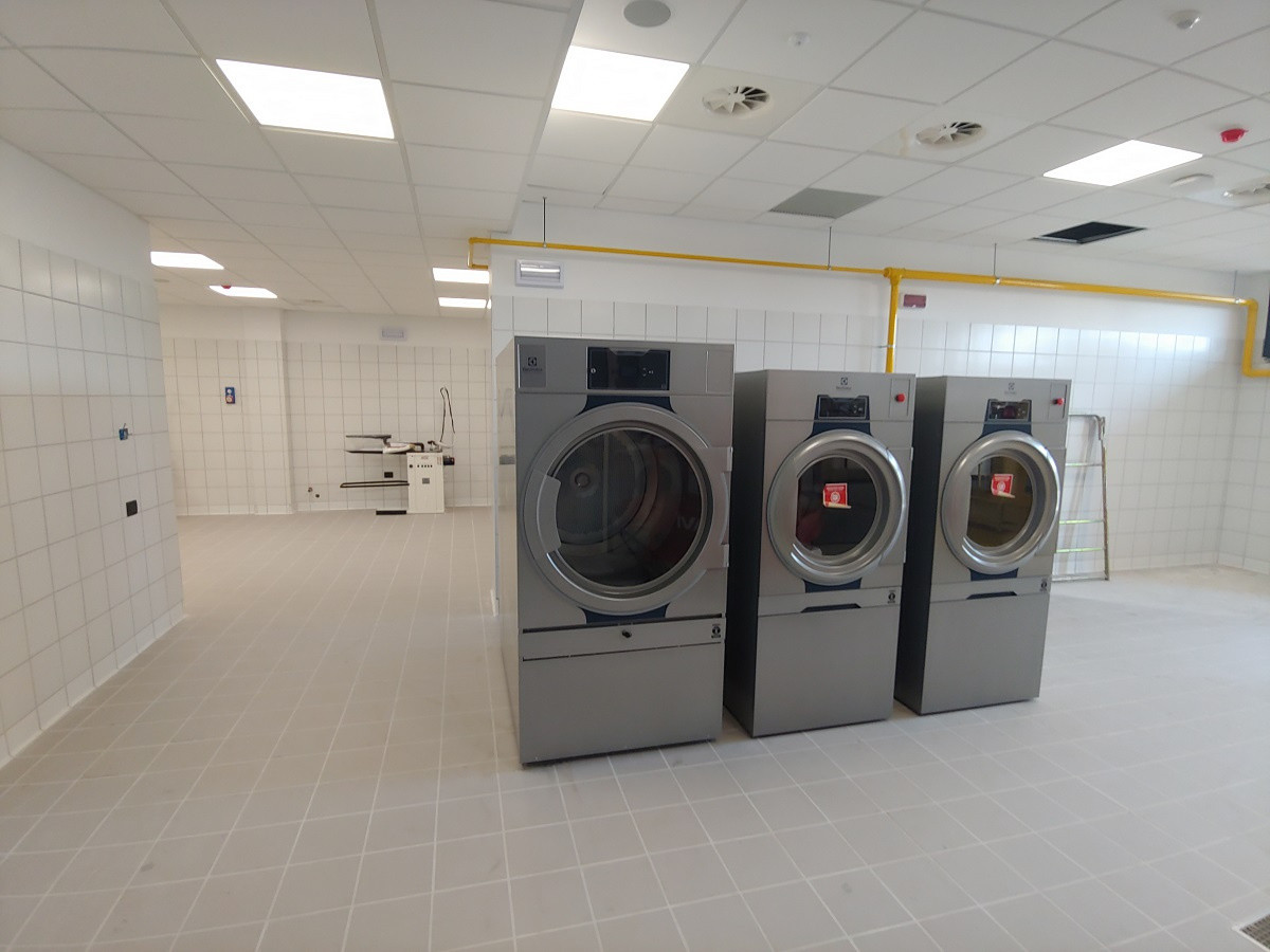 Vista interna dell'Edificio 8: Lavanderia, lavatrici industriali in acciaio in primo piano