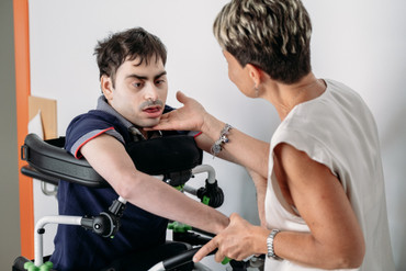 Simone e la sua educatrice sono a passeggio nei corridoi della Lega del Filo d'Oro. L'educatrice accarezza il viso di Simone