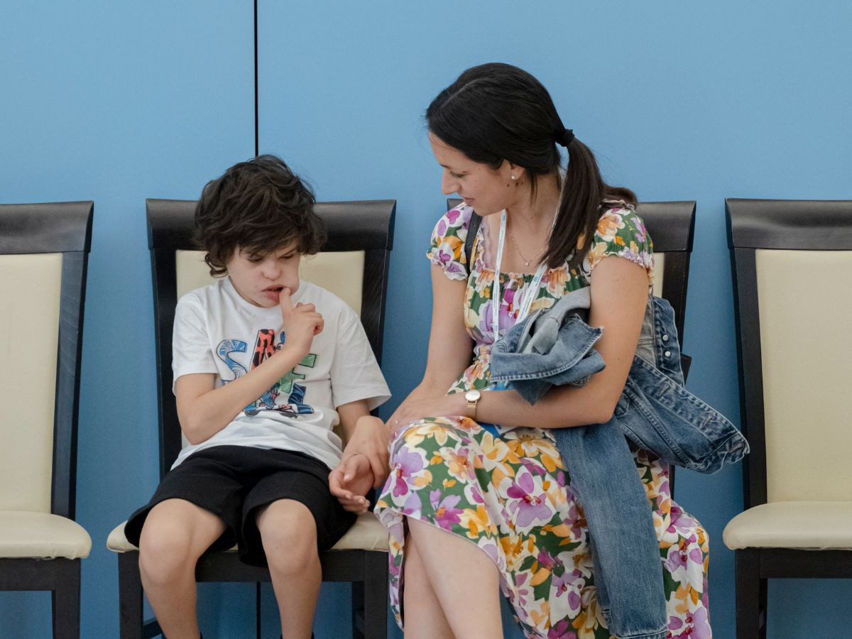 La volontaria Arianna siede vicino al piccolo Agostino e si tengono per mano