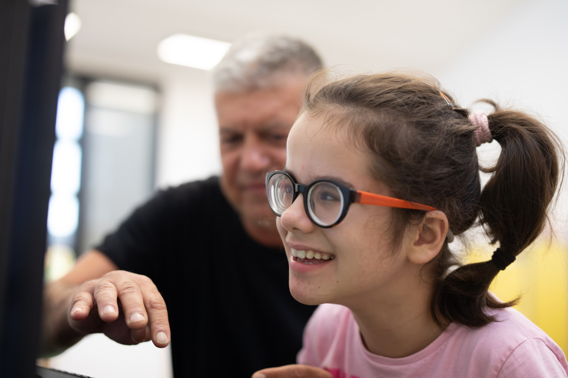 Una bambina, utente della Lega del Filo d'Oro, lavora al computer aiutata dall'educatore