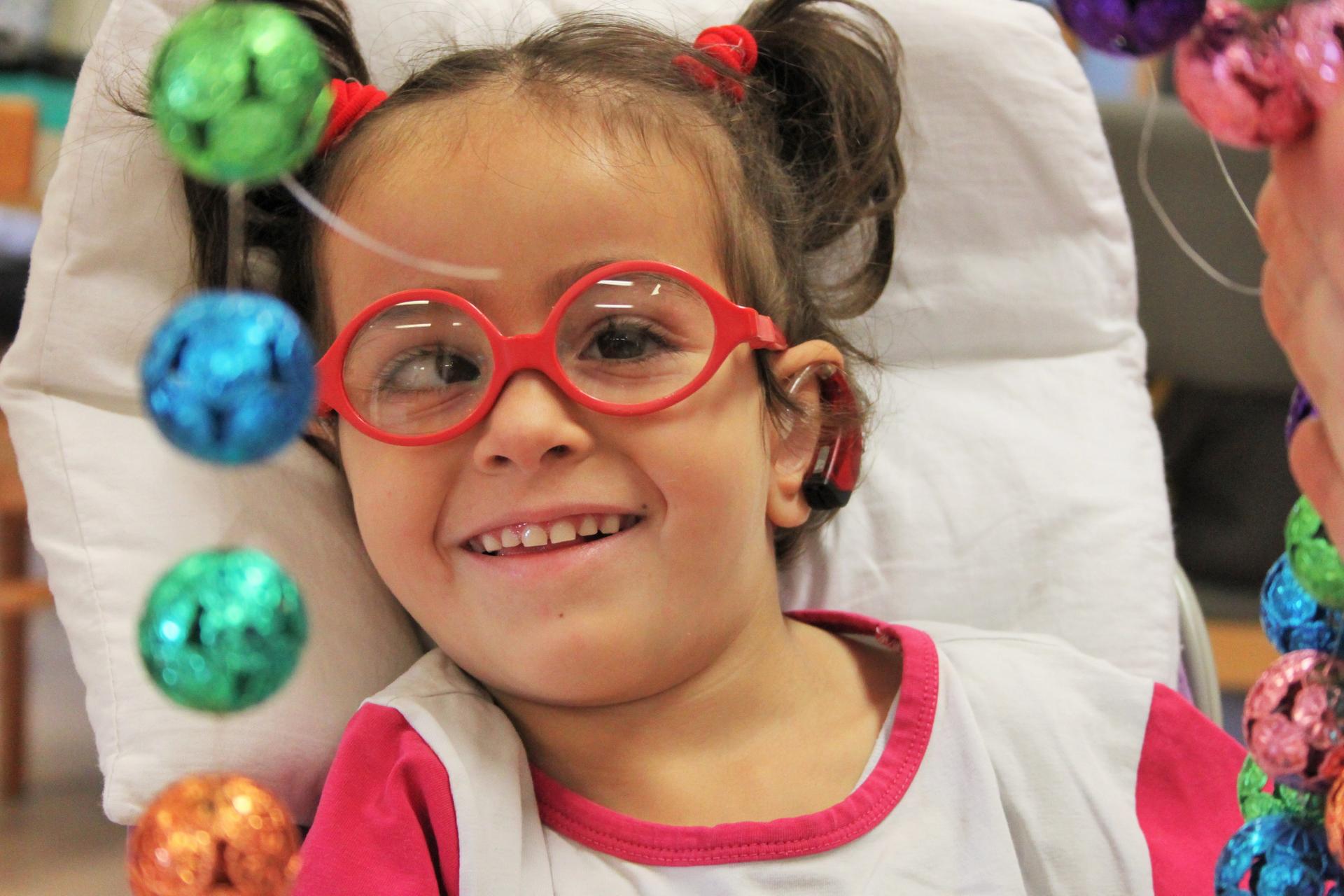 La piccola sofia sorride mentre con l'educatrice svolge un'attività di stimolazione sensoriale: toccare un telaio con appesi tanti sonagli colorati