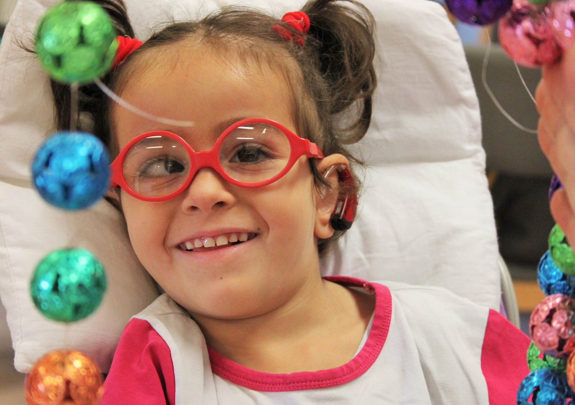 La piccola sofia sorride mentre con l'educatrice svolge un'attività di stimolazione sensoriale: toccare un telaio con appesi tanti sonagli colorati