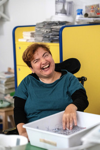 Una ragazza utente della Lega del Filo d'Oro divertita, mentre gioca con dei coriandoli di carta in una bacinella bianca 