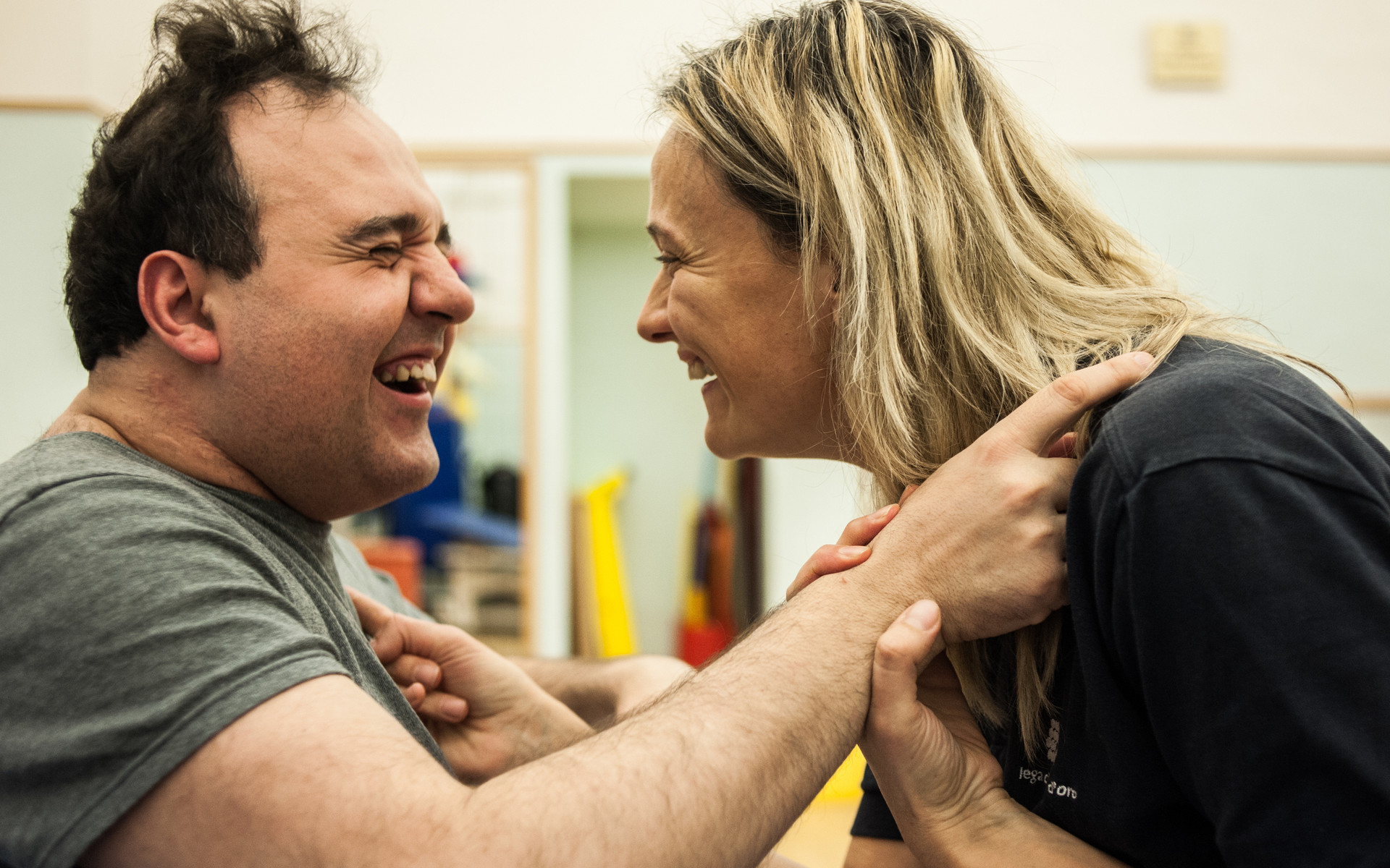Alberto, utente adulto del Centro di Osimo della Lega del Filo d'Oro, ride divertito insieme alla fisioterapista. Foto di profilo dei due faccia a faccia