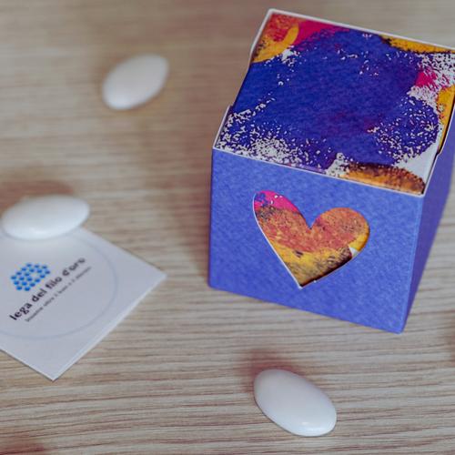 Bomboniera Cubo Pop composta da due scatoline in cartoncino pregiato inserite l'una nell'altra. Quella esterna è blu, quella interna, visibile da un'apertura a forma di cuore, ha una fantasia multicolore ispirata ai disegni degli ospiti della Lega del Filo d'Oro 17
