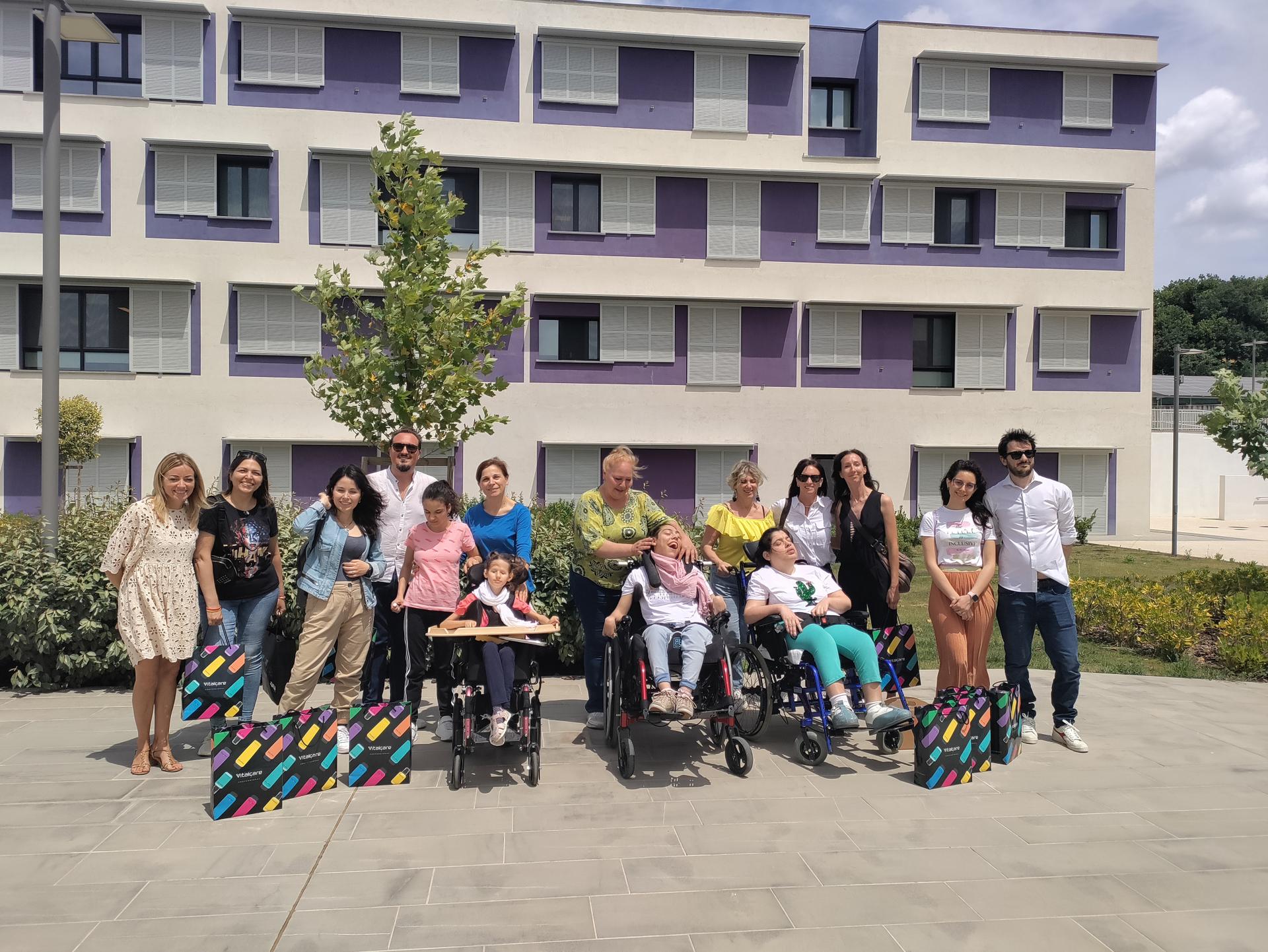 Quindici persone tra team Sodico e utenti sorridono durante il “Beauty Day” al Centro Nazionale di Osimo. Alle loro spalle, la palazzina bianca e viola della sede della Lega del Filo d’Oro di Osimo.
