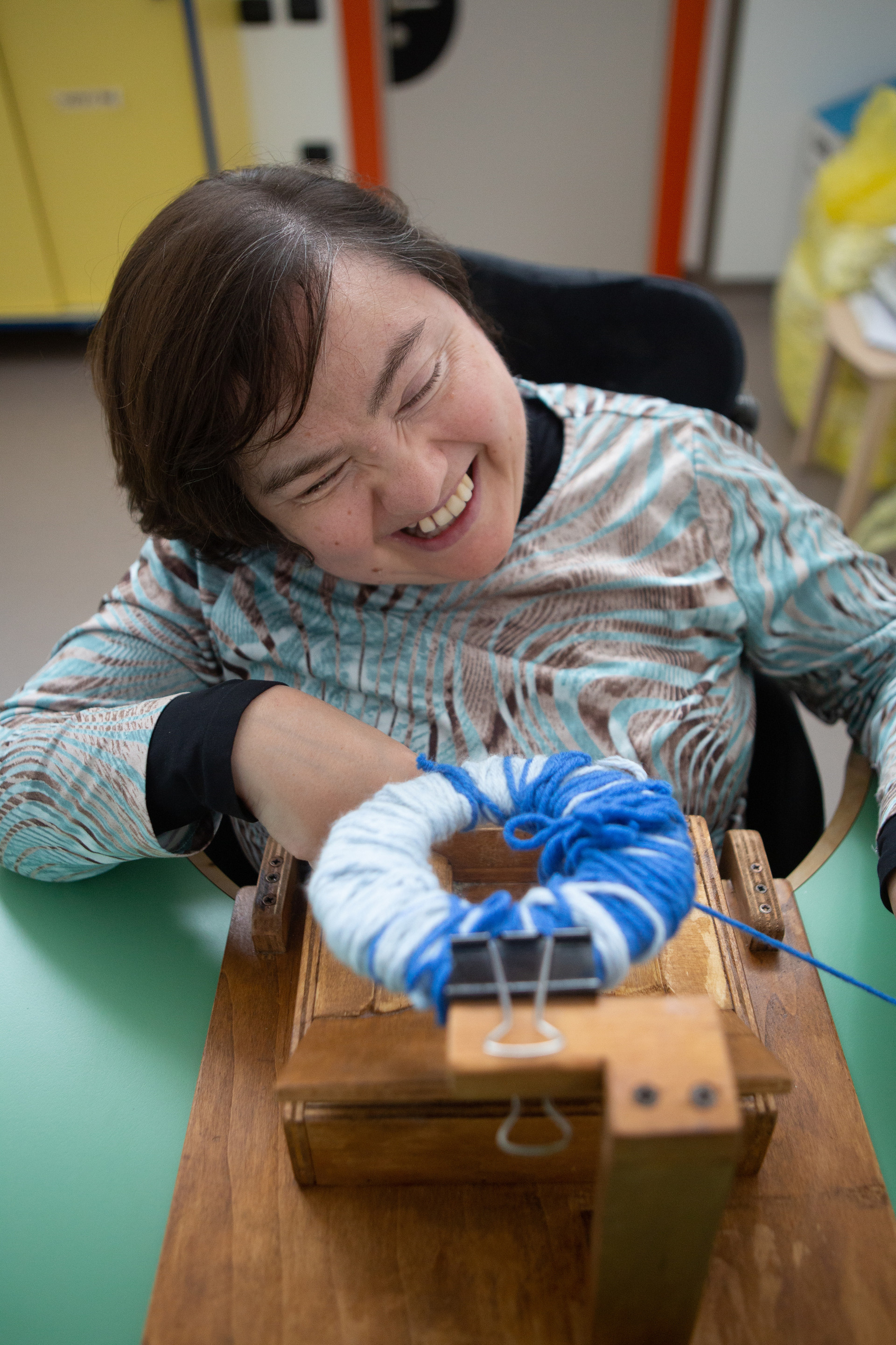 Paola, utente adulta del Centro Nazionale della Lega del Filo d’Oro, è ritratta mentre realizza un pompon azzurro e celeste con l’apposito strumento.